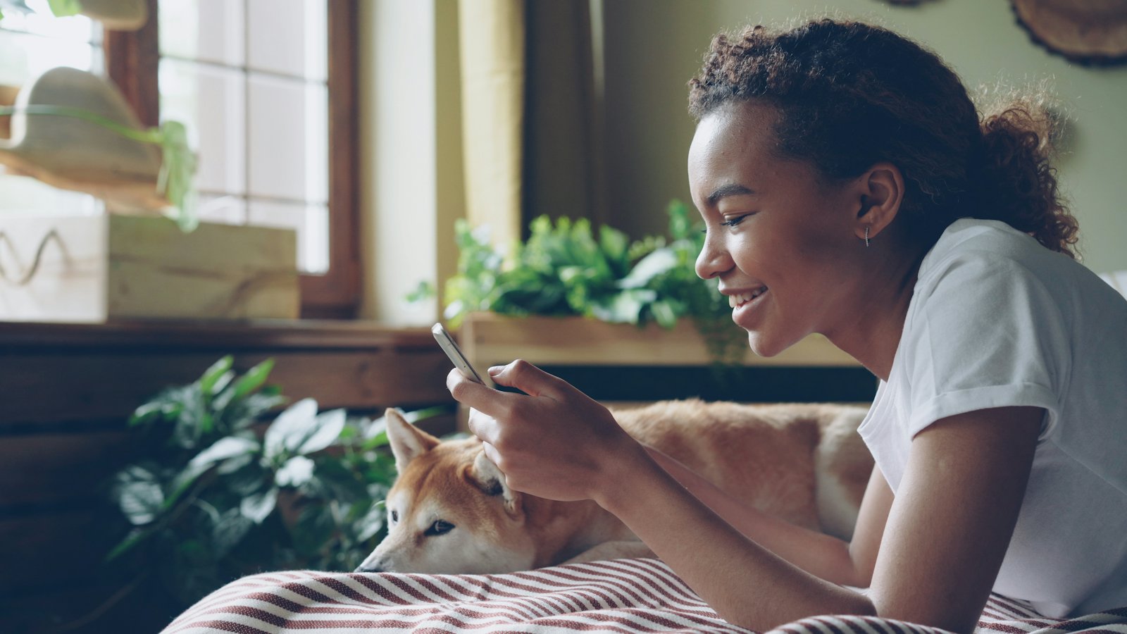 A woman smiles at her phone while her dog rests beside her.